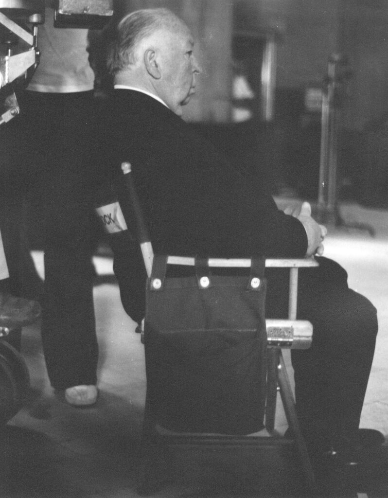 Alfred Hitchcock am Set eines seiner Filme um 1960, mit ernstem Blick in die Kamera, die Silhouette seines Profils deutlich erkennbar.