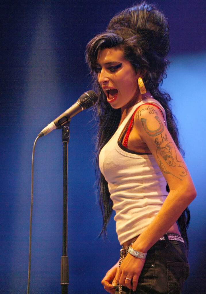 Amy Winehouse mit ihrer markanten Beehive-Frisur und dem typischen dicken Lidstrich während eines Live-Auftritts um das Jahr 2007.