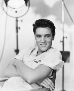 Elvis Presley während eines Live-Auftritts Mitte der 1950er Jahre, in charakteristischer Pose mit seiner Akustikgitarre.