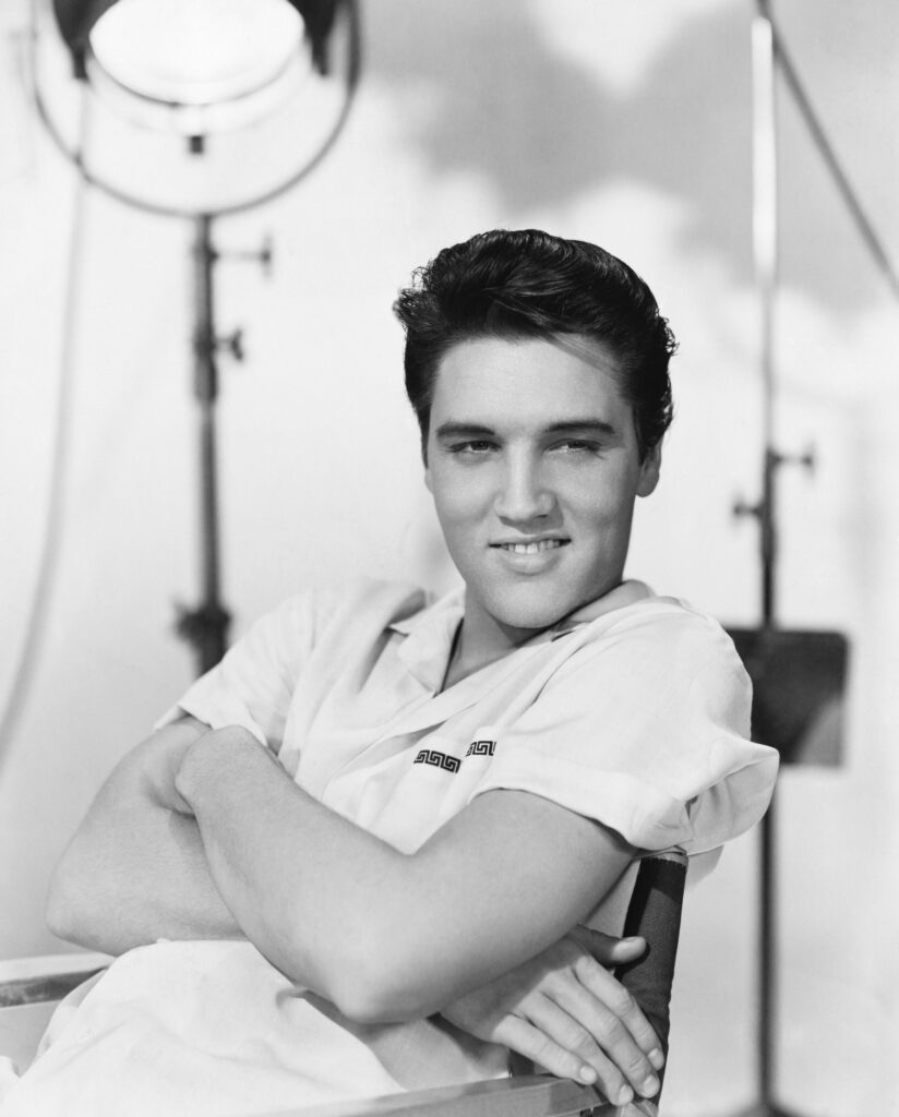 Elvis Presley während eines Live-Auftritts Mitte der 1950er Jahre, in charakteristischer Pose mit seiner Akustikgitarre.