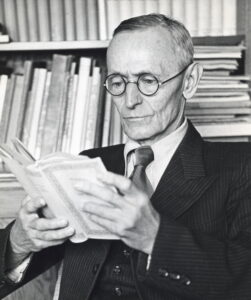 Hermann Hesse in seinem Garten in Montagnola, um 1950, mit Hut und Brille in nachdenklicher Pose sitzend.