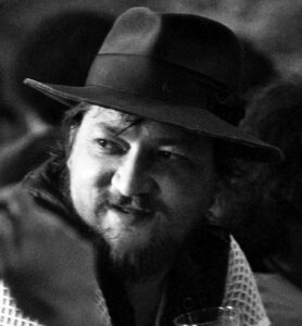 Rainer Werner Fassbinder in den späten 1970er Jahren, nachdenklich mit Zigarette, eine typische Pose des exzessiv arbeitenden Regisseurs.