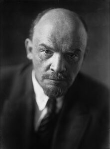Wladimir Iljitsch Lenin auf einer Fotografie um 1920, mit ernstem Blick, Anzug und Weste, eine Hand in der Tasche haltend.