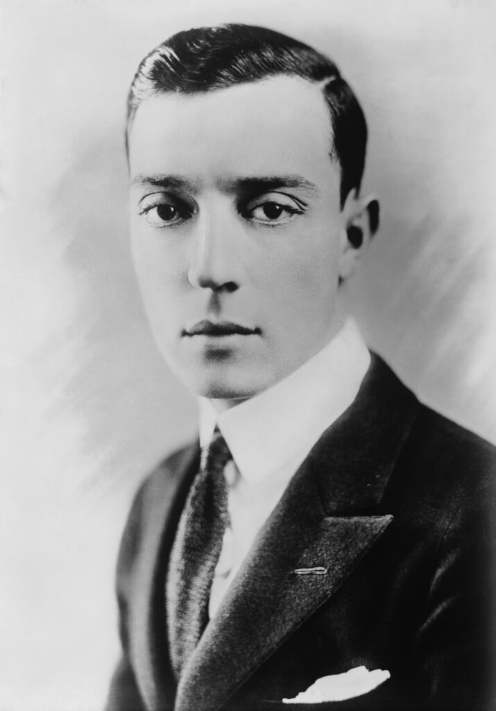 Buster Keaton mit seinem typischen Porkpie-Hut und ernstem Gesichtsausdruck in einer Studioaufnahme aus den 1920er-Jahren.