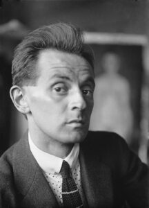 Der österreichische Expressionist Egon Schiele in einer Atelieraufnahme um 1914, mit konzentriertem Blick und charakteristischer Kleidung.