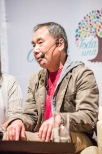 Der japanische Schriftsteller Haruki Murakami sitzt nachdenklich in einem Sessel, umgeben von Büchern und Schallplatten, in einer undatierten Aufnahme.