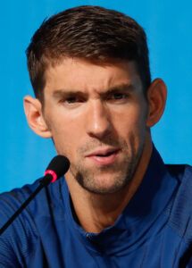 Der US-Schwimmer Michael Phelps konzentriert sich vor einem Start bei den Olympischen Spielen, seine Schwimmbrille auf der Kappe, der Blick fokussiert.
