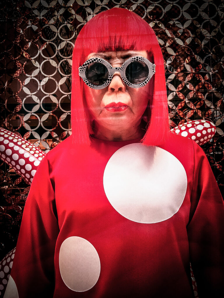 Yayoi Kusama in ihrem Atelier in Tokio, umgeben von Werken der Serie 'My Eternal Soul', erkennbar an den leuchtenden Farben und Mustern.