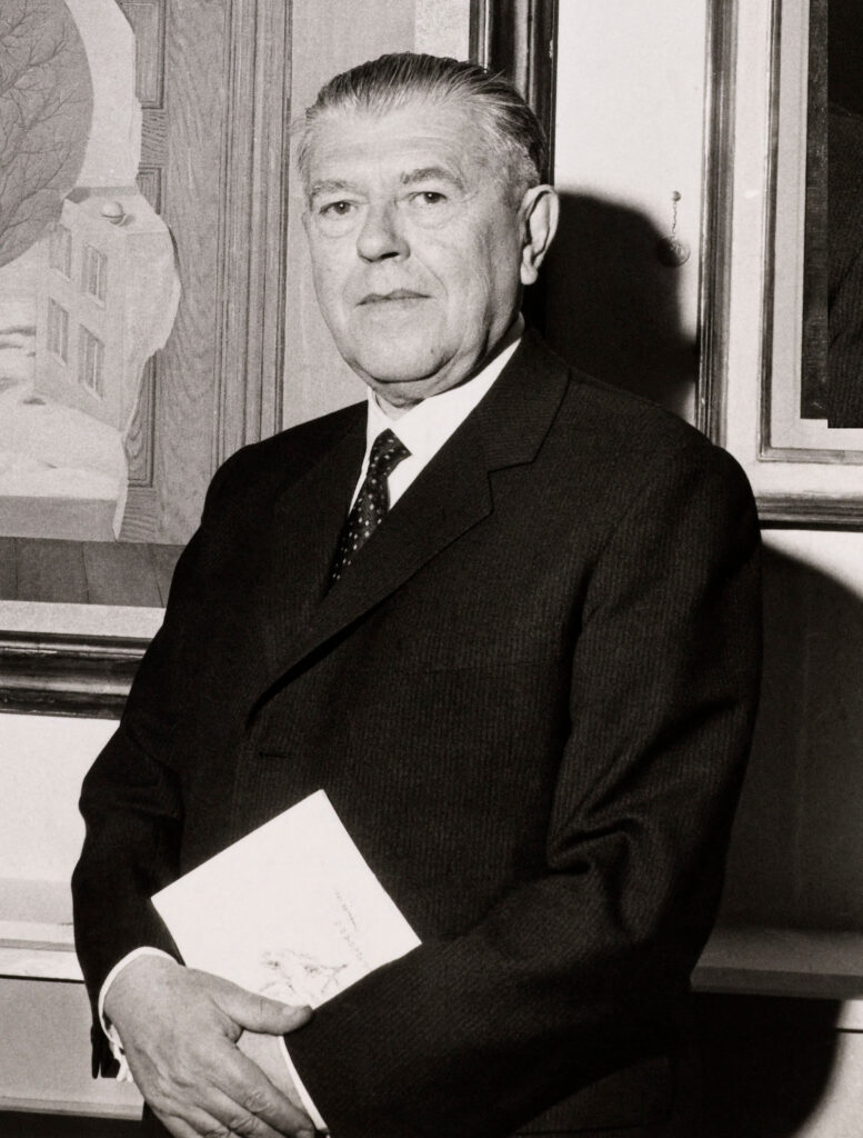 Der belgische Surrealist René Magritte in seinem Brüsseler Atelier, stehend neben einer Staffelei, umgeben von seinen ikonischen Gemälden, eine undatierte Aufnahme.