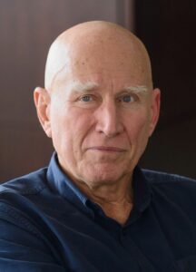 Der Fotograf Sebastião Salgado bei einer Ausstellungseröffnung, in schwarzweiß gehalten, mit einer seiner großformatigen Fotografien im Hintergrund.