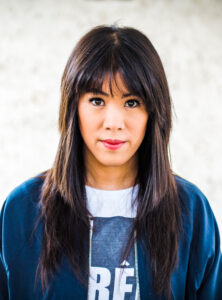 Die Wissenschaftsjournalistin Mai Thi Nguyen-Kim gestikuliert während eines Vortrags auf einer Bühne, im Hintergrund eine Projektion.