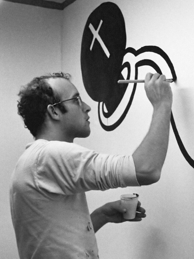 Der Künstler Keith Haring bei der Arbeit an einem seiner Wandgemälde, konzentriert mit einem Pinsel in der Hand, um 1986.