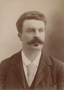 Eine Fotografie von Guy de Maupassant um 1888, der französische Schriftsteller blickt mit ernstem Ausdruck und markantem Schnurrbart direkt in die Kamera.