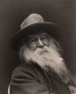 Der Dichter Walt Whitman in einer Porträtaufnahme um 1887, mit langem weißem Bart und Hut, sein Blick ist direkt in die Kamera gerichtet.