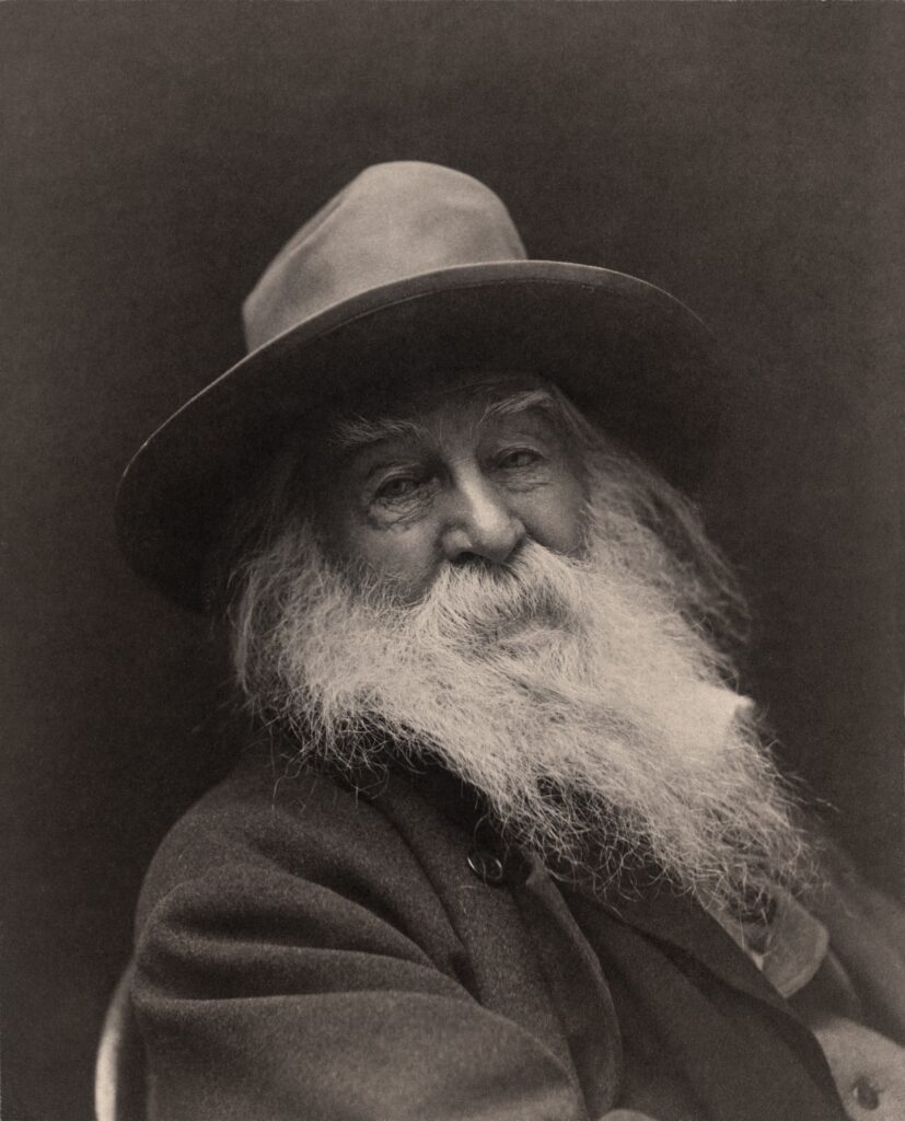 Der Dichter Walt Whitman in einer Porträtaufnahme um 1887, mit langem weißem Bart und Hut, sein Blick ist direkt in die Kamera gerichtet.